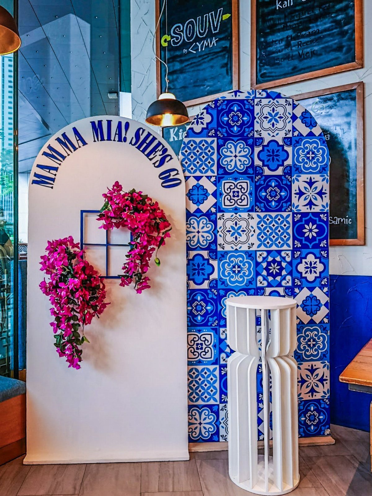 Party backdrop with a white arch, pink flowers, and blue patterned tiles.