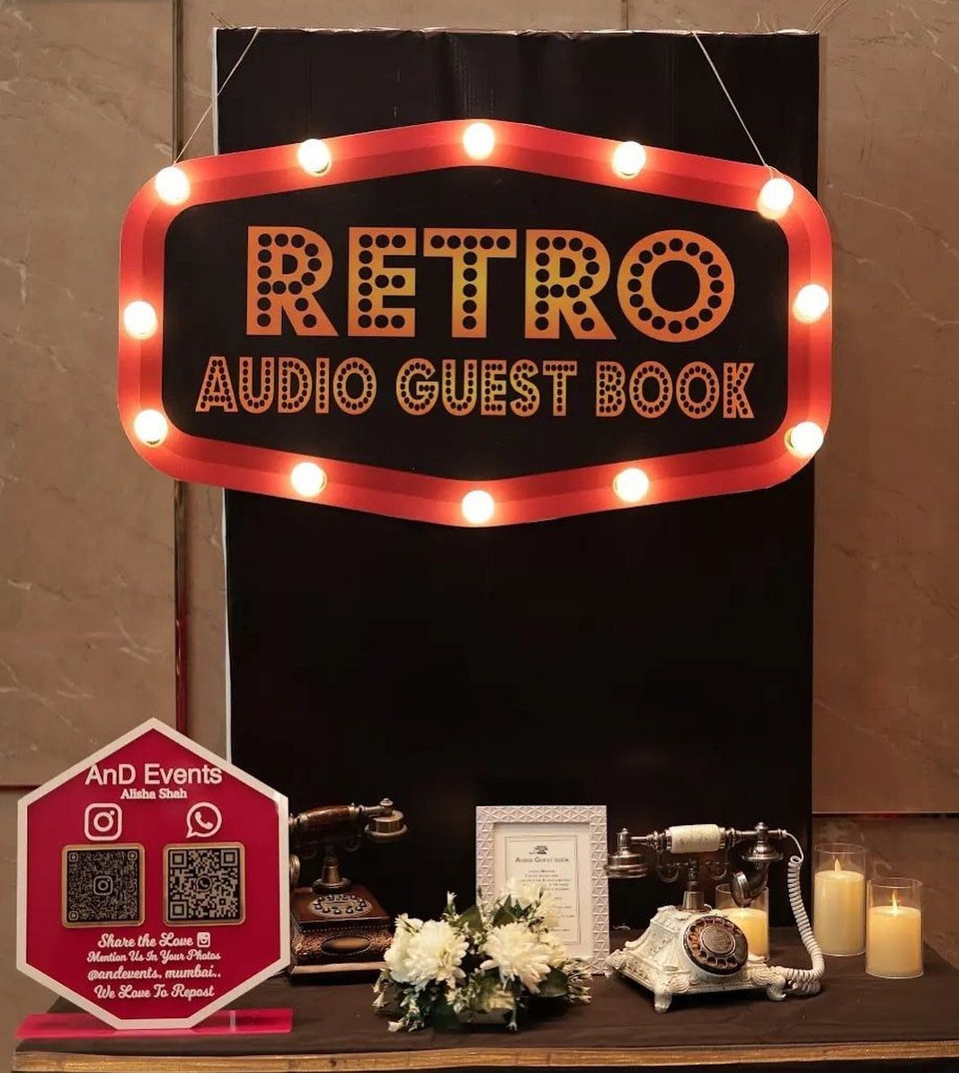 Retro audio guest book setup with illuminated sign, vintage telephones, and white flowers.