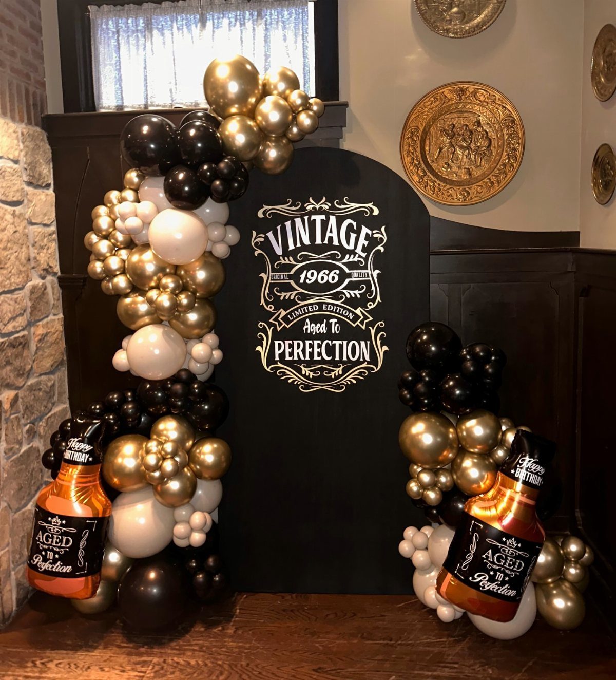 Black backdrop with vintage 1966 text surrounded by gold and black balloons.
