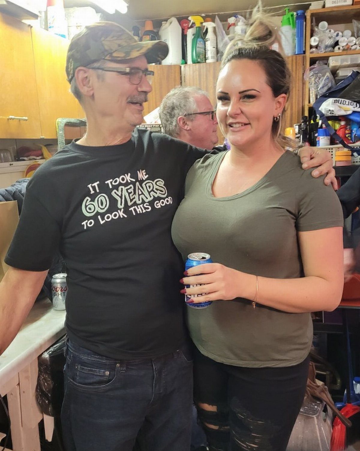 Man in 60th birthday shirt and woman posing together in a kitchen.