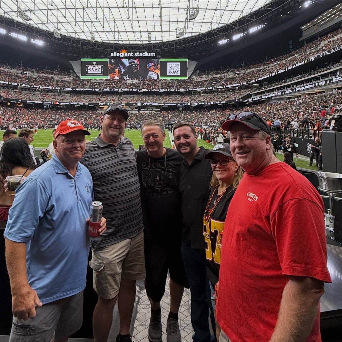 Group of adults posing for a photo inside Allegiant Stadium during a game.
