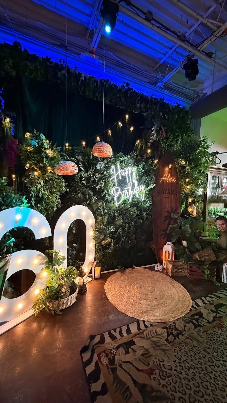 Illuminated number 60 and neon birthday sign surrounded by tropical plants and foliage.