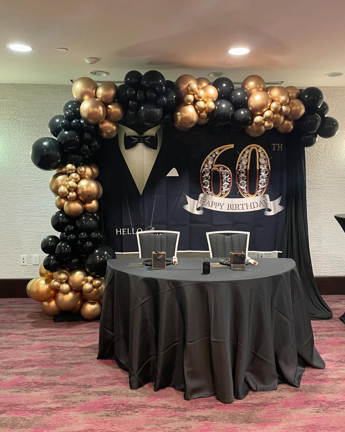 Tuxedo themed 60th birthday party decoration with black and gold balloon arch.