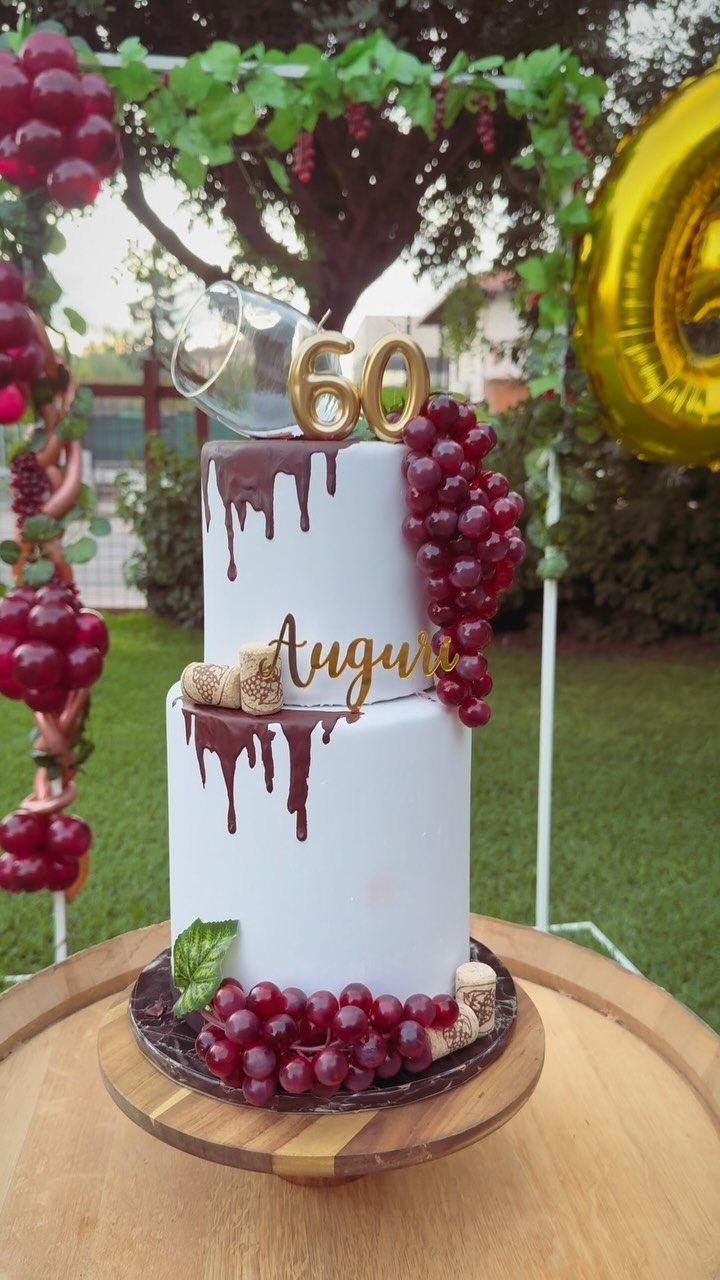 Two-tier white birthday cake with chocolate drips, red grapes, and gold 60 topper.
