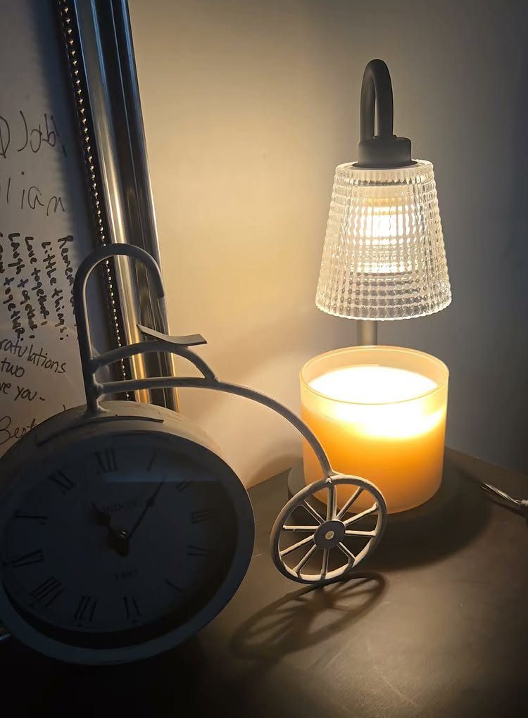 Candle warmer lamp with glass shade heating a yellow candle beside a bicycle clock