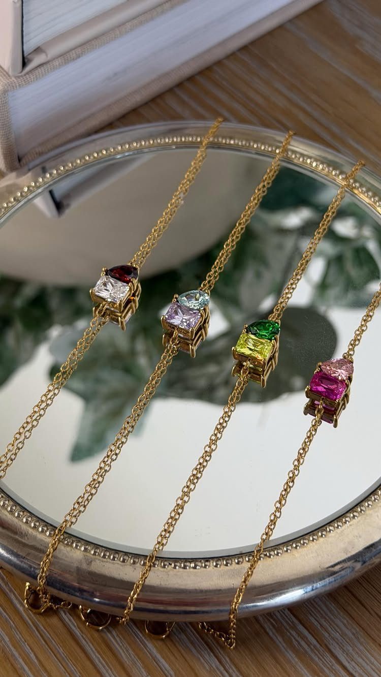 Four gold heart-shaped gemstone necklaces displayed on a round mirror tray.