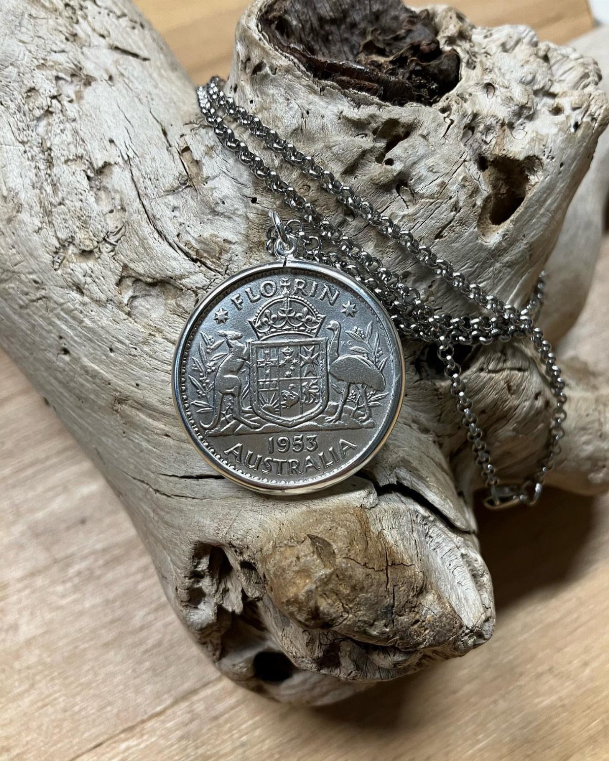 Silver 1953 Australian florin coin pendant on a chain resting on driftwood