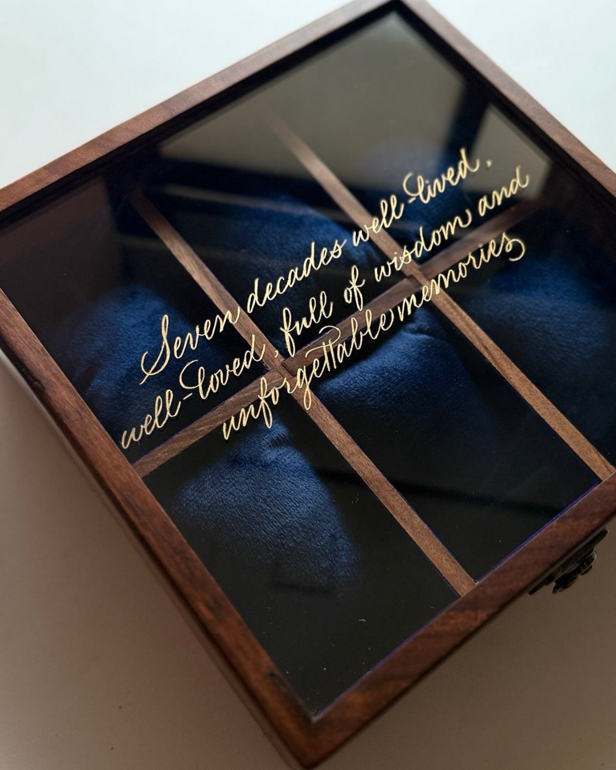 Wooden watch box with glass lid and gold cursive inscription on blue velvet.