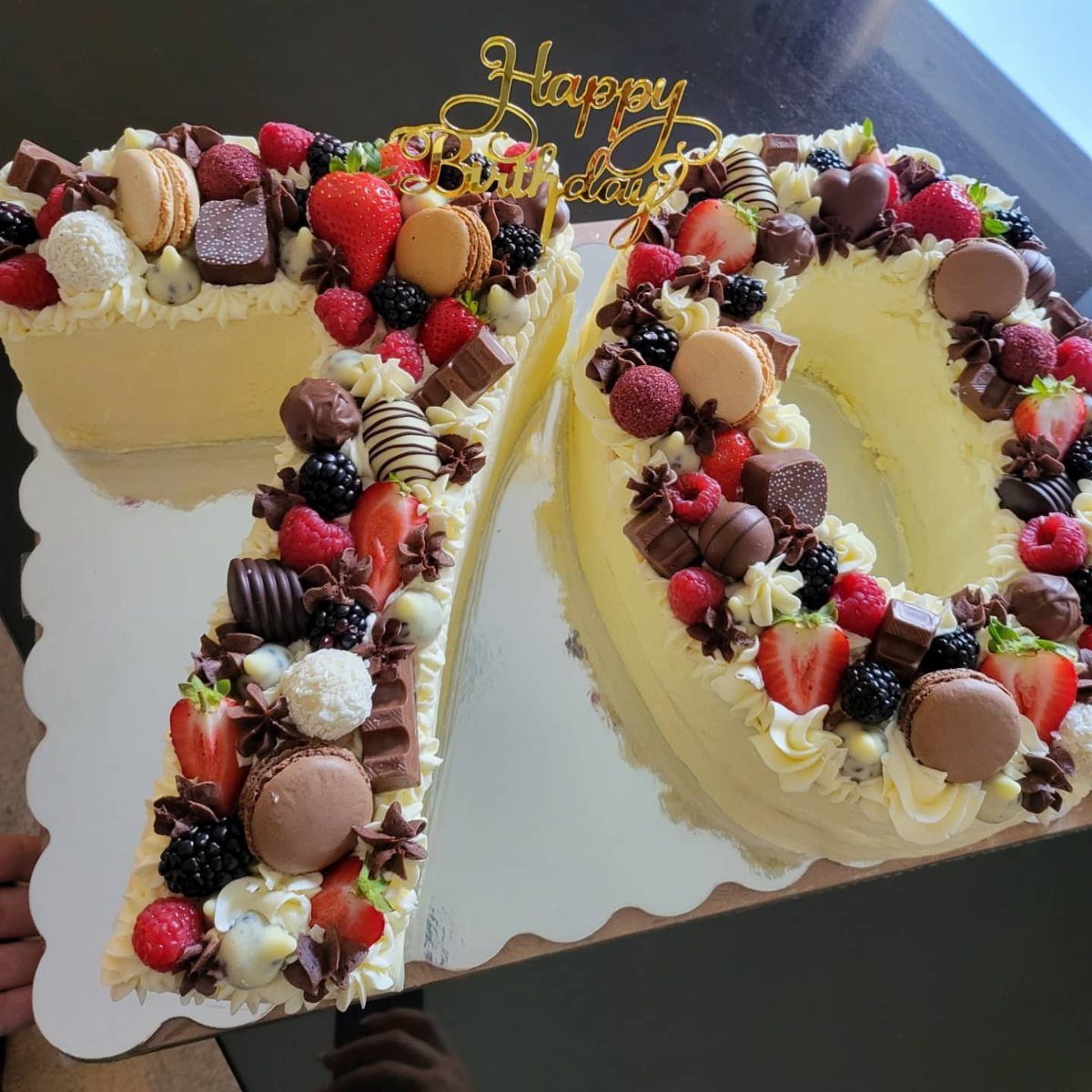 Number 70 birthday cake decorated with fresh berries, macarons, and chocolate pieces.
