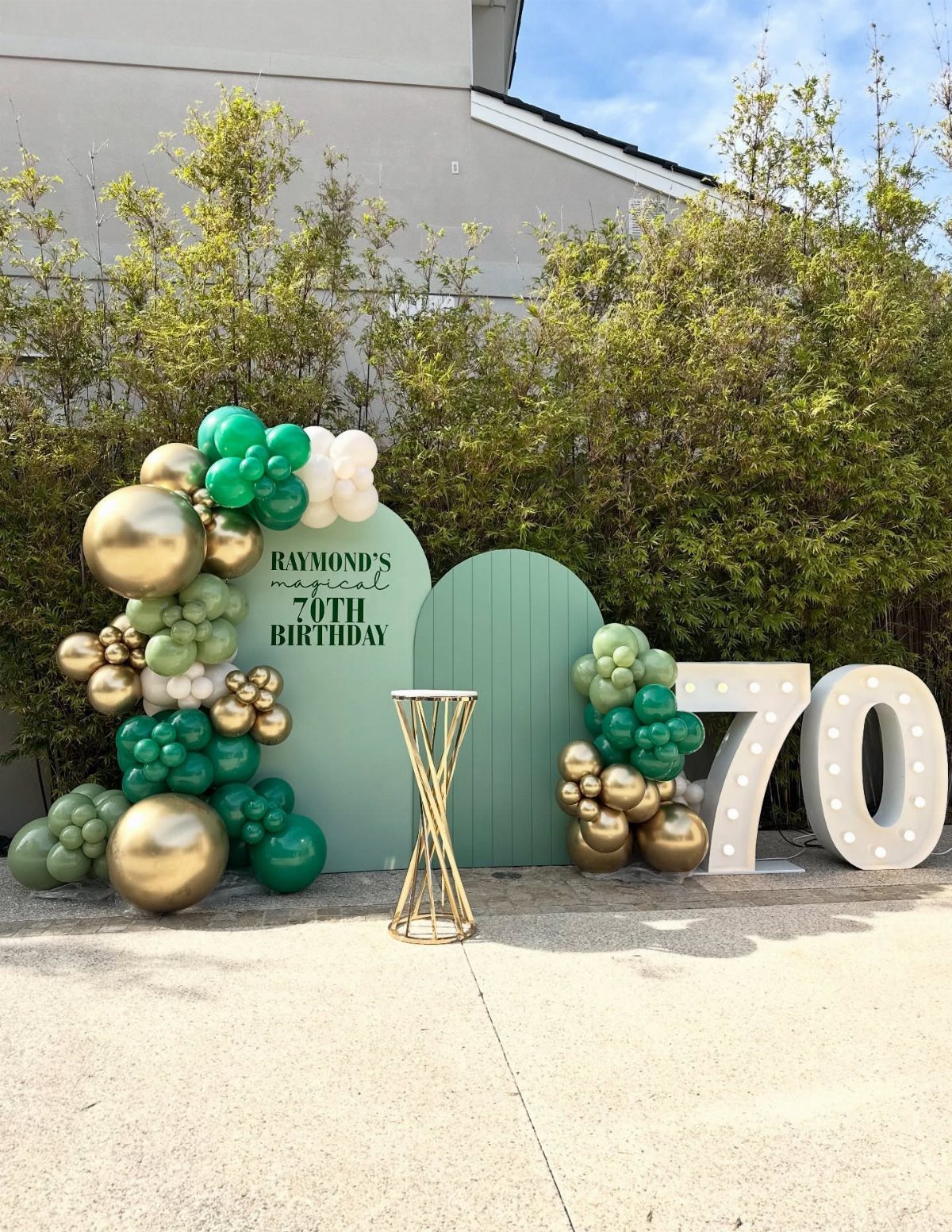 70th birthday party decoration with green and gold balloons and large illuminated numbers.