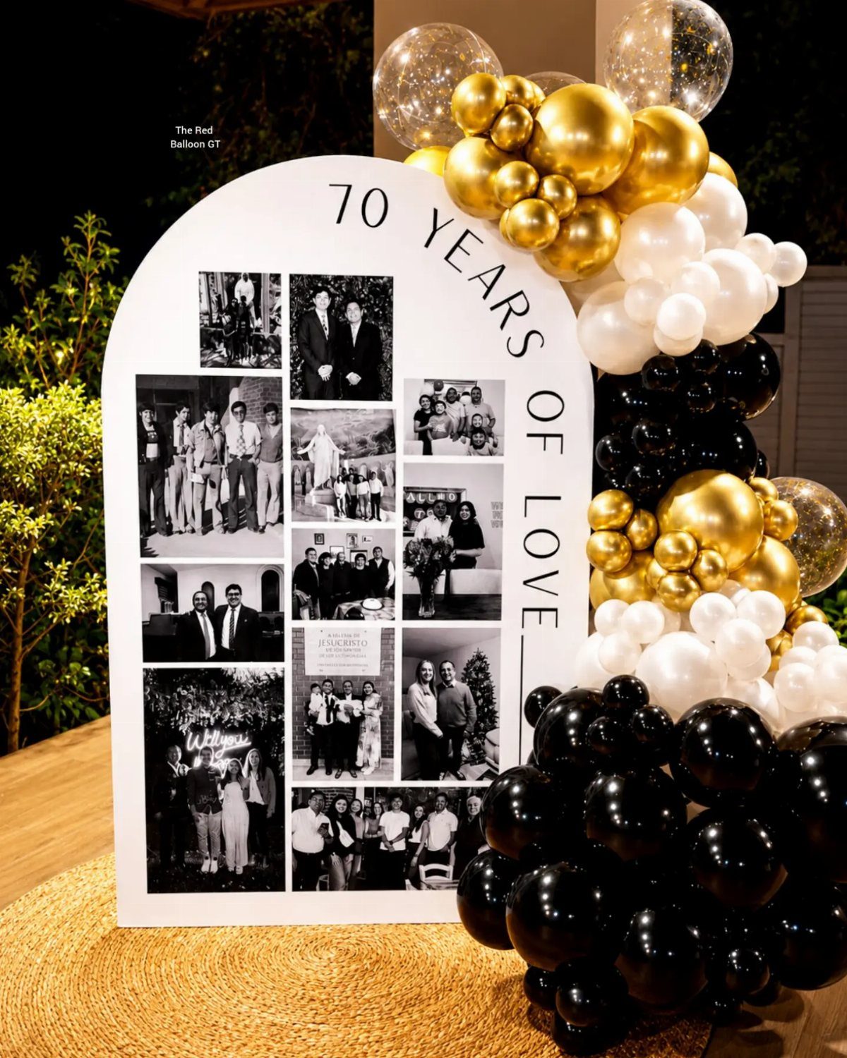 Arched photo display board with black and white family pictures and gold balloons.