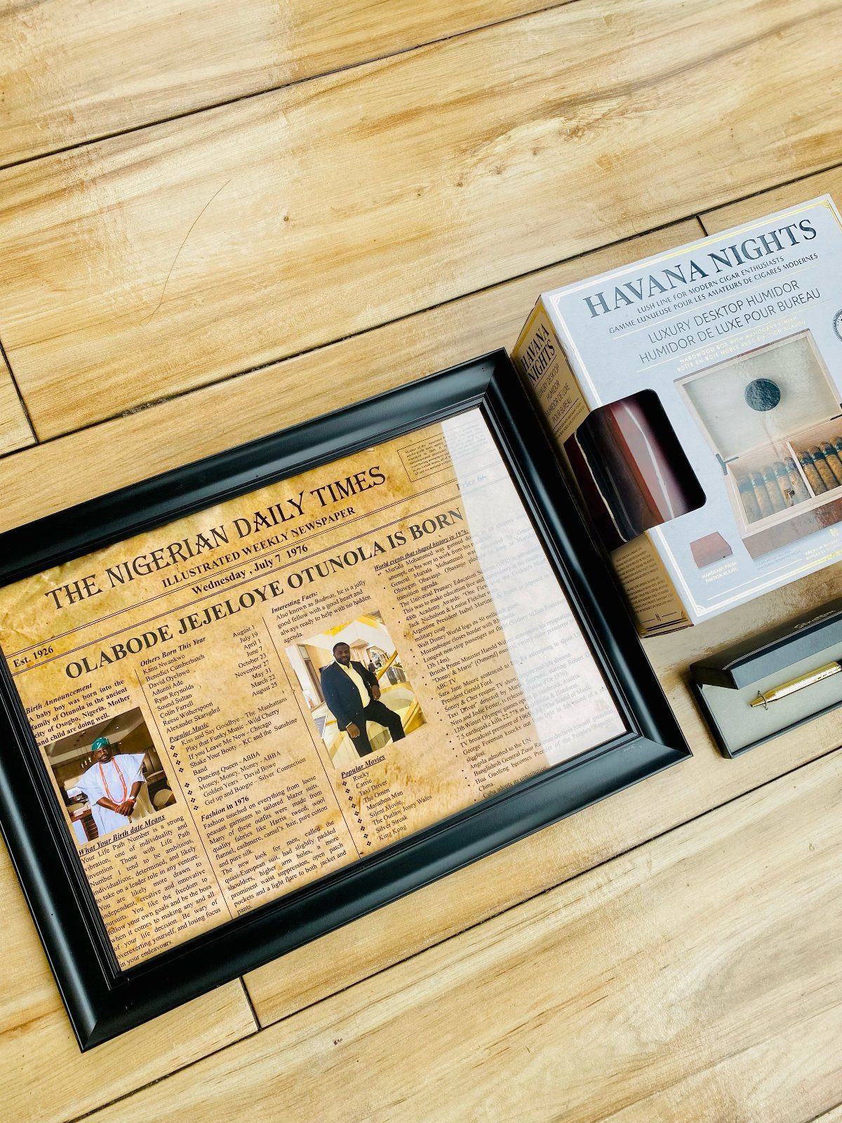Framed personalized newspaper page celebrating a birth, placed on a wooden floor.