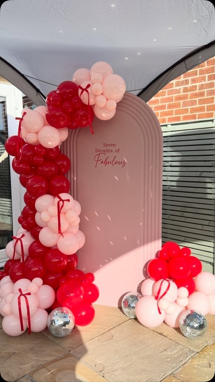 Pink arched backdrop with red and pink balloons and silver disco balls.