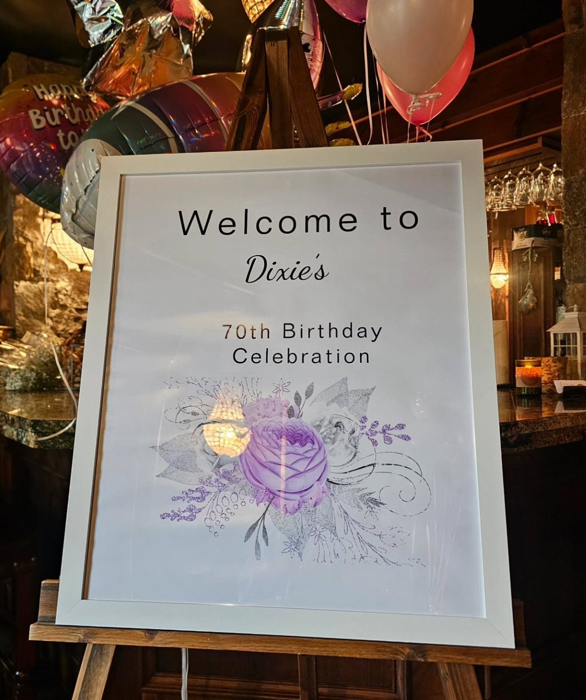 Welcome sign for Dixie's 70th birthday celebration on a wooden easel with balloons.