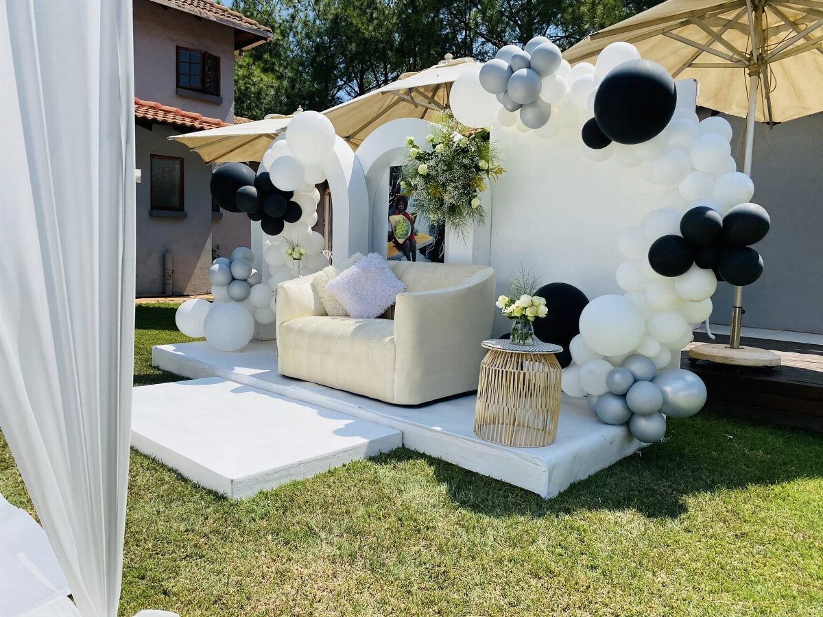 Outdoor party setup with a cream armchair and white and black balloon arch.