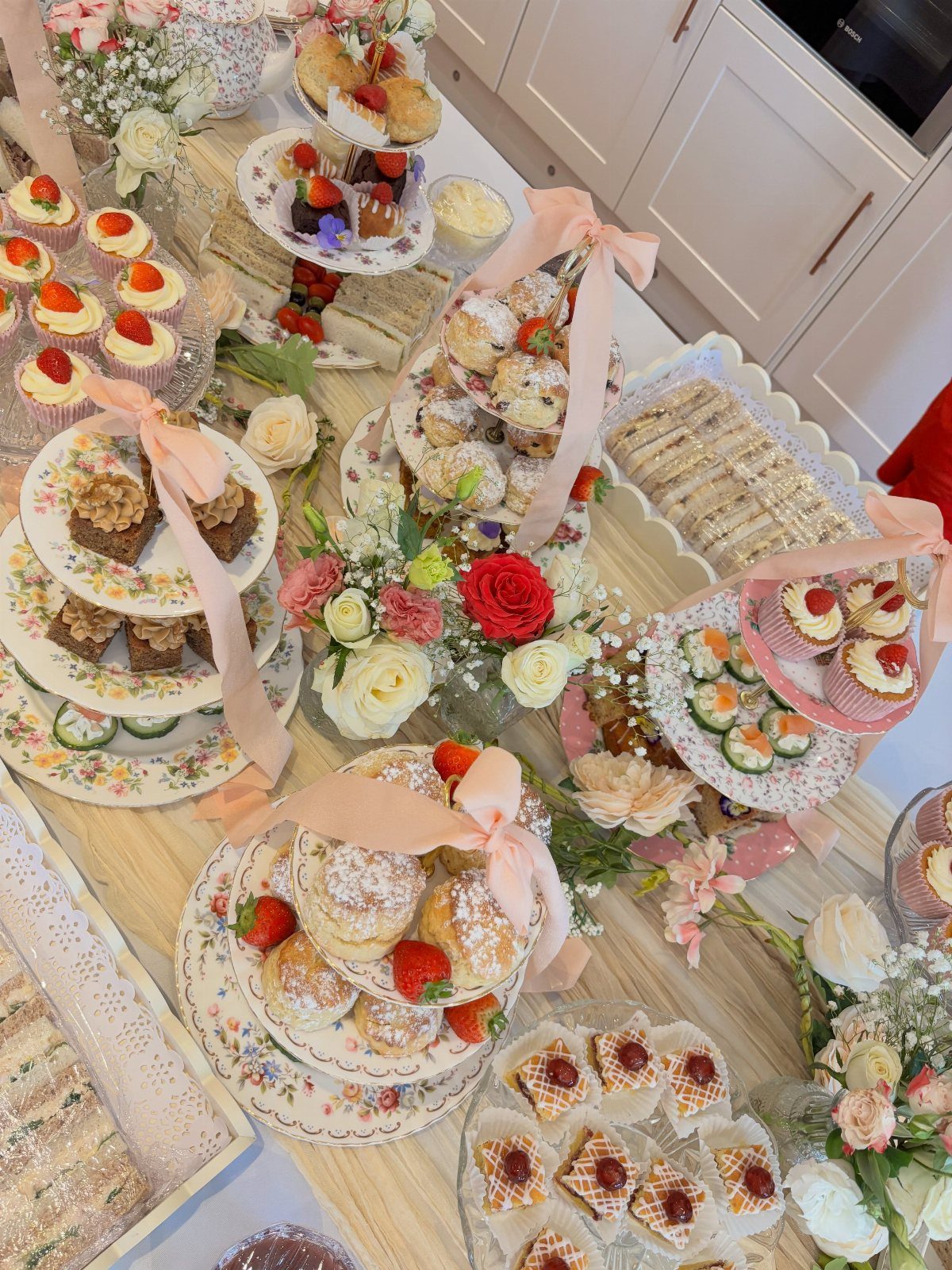 Elegant high tea spread with tiered cake stands, pastries, sandwiches, and fresh flowers.