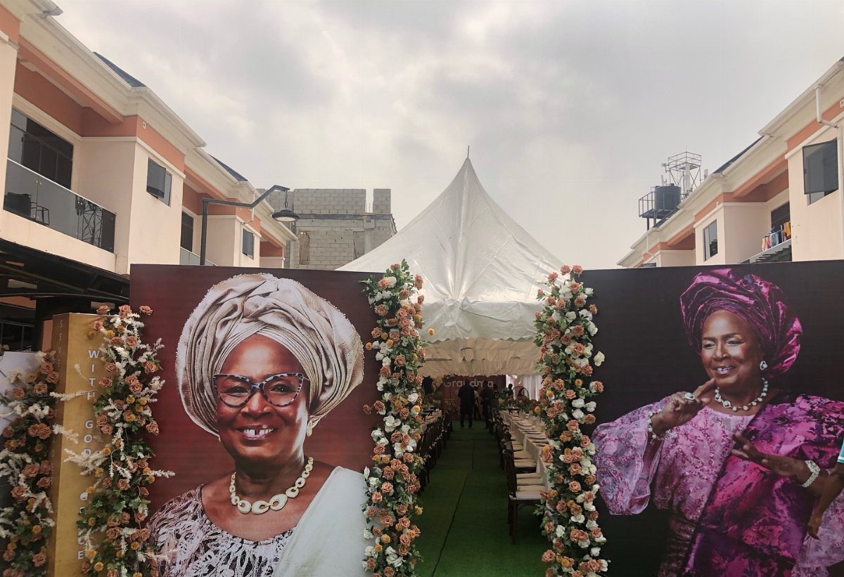 Outdoor party setup with large portraits of a woman and floral pillars.