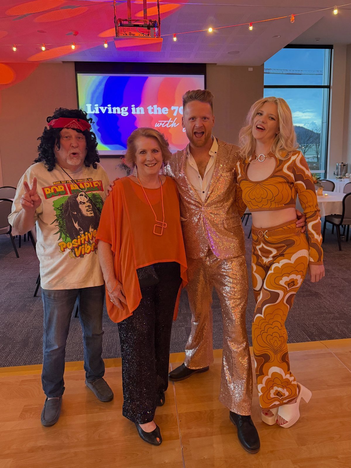 Four people wearing 1970s themed costumes posing in front of a party screen.