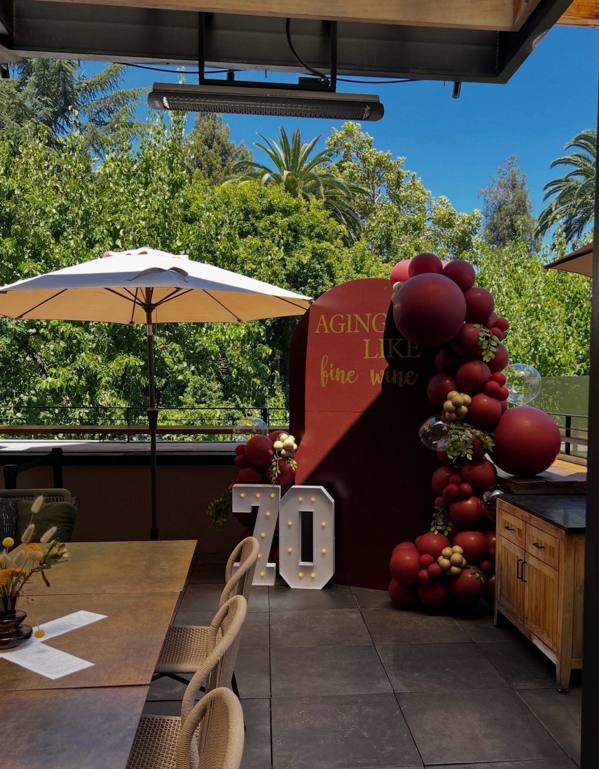 Burgundy birthday backdrop with gold text and balloons next to light-up 70 numbers.