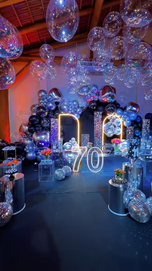 Glowing number 70 sign surrounded by silver disco balls and blue balloons.