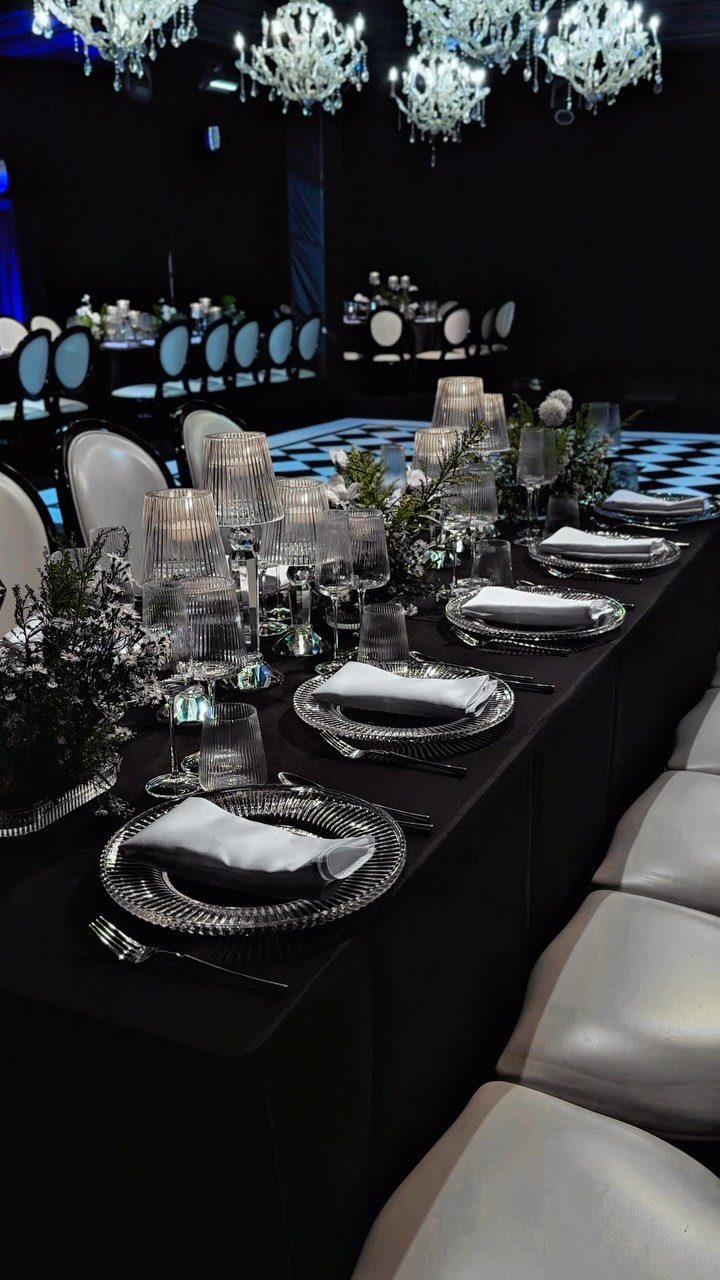 Elegant black and white dinner table setting with crystal chandeliers and silver plates.
