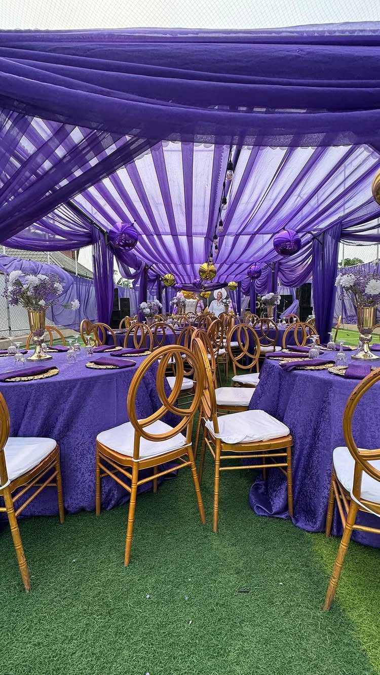 Purple draped event tent with gold chairs and tables on green grass