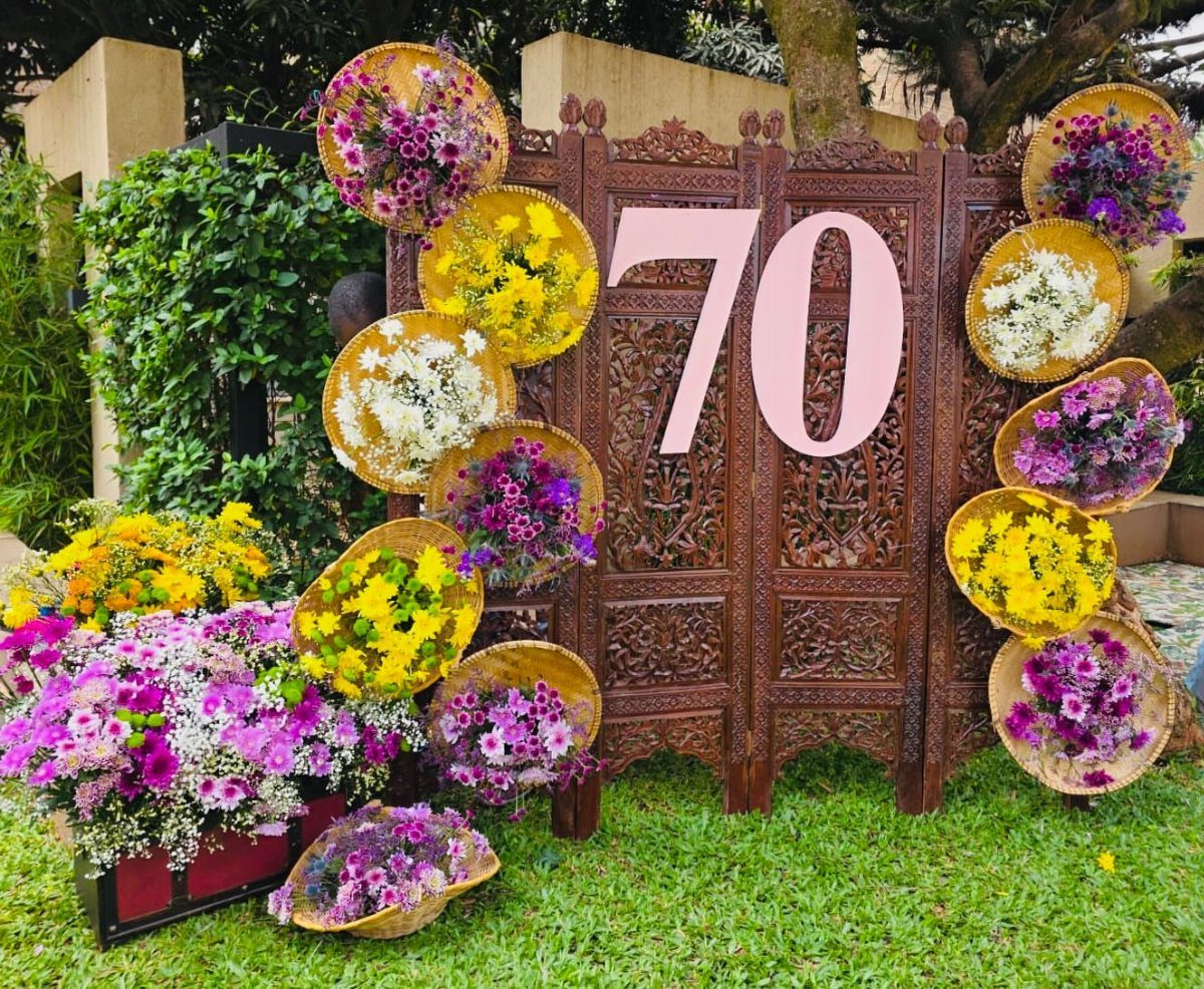 Carved wooden backdrop with pink number 70 and colorful circular floral arrangements outdoors