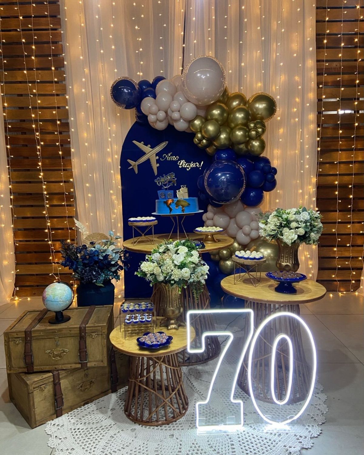 Travel themed 70th birthday party decor with vintage suitcases, globe, and glowing number 70.