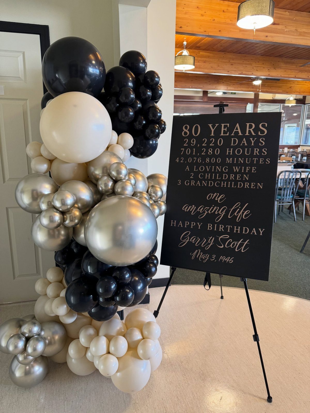 Black chalkboard birthday sign and gold, black, and cream balloon arch decoration.