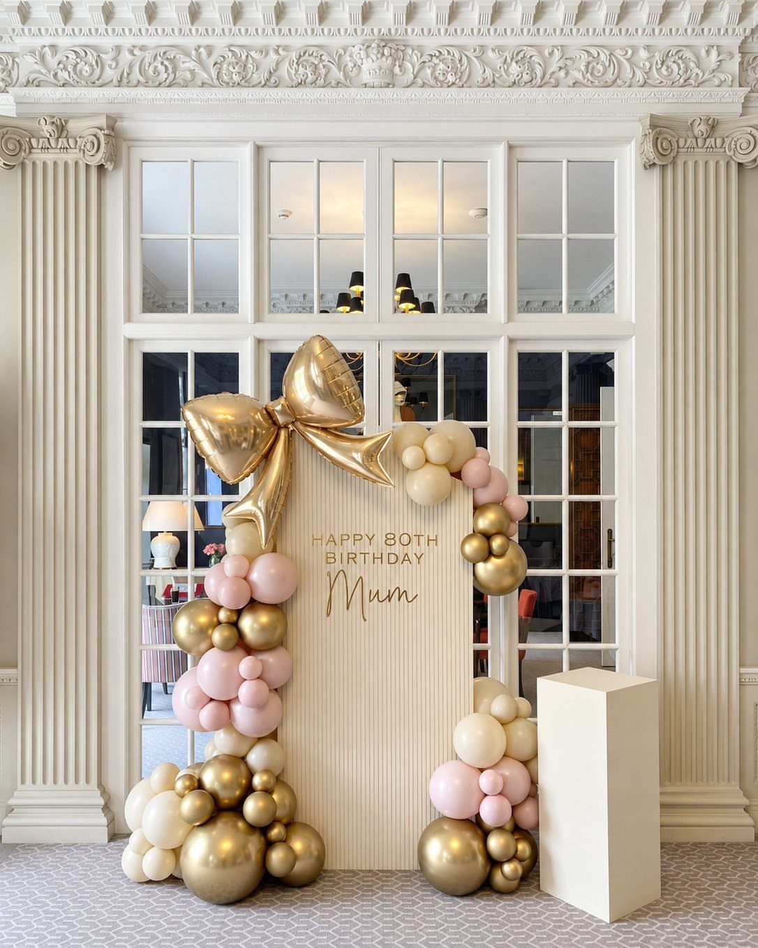 Arched birthday backdrop with gold and pink balloons and a large gold bow.