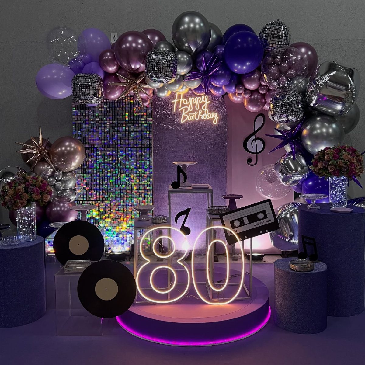 Purple and silver 80th birthday party decoration with glowing numbers and musical elements.