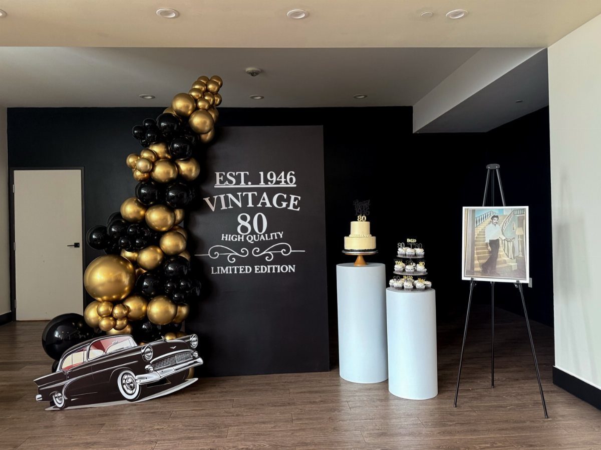 Vintage 80th birthday party decoration with black and gold balloons and a cake.