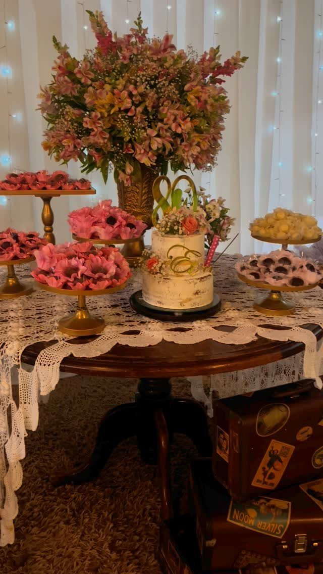 Dessert table with 80th birthday cake, pink treats, and vintage suitcases.
