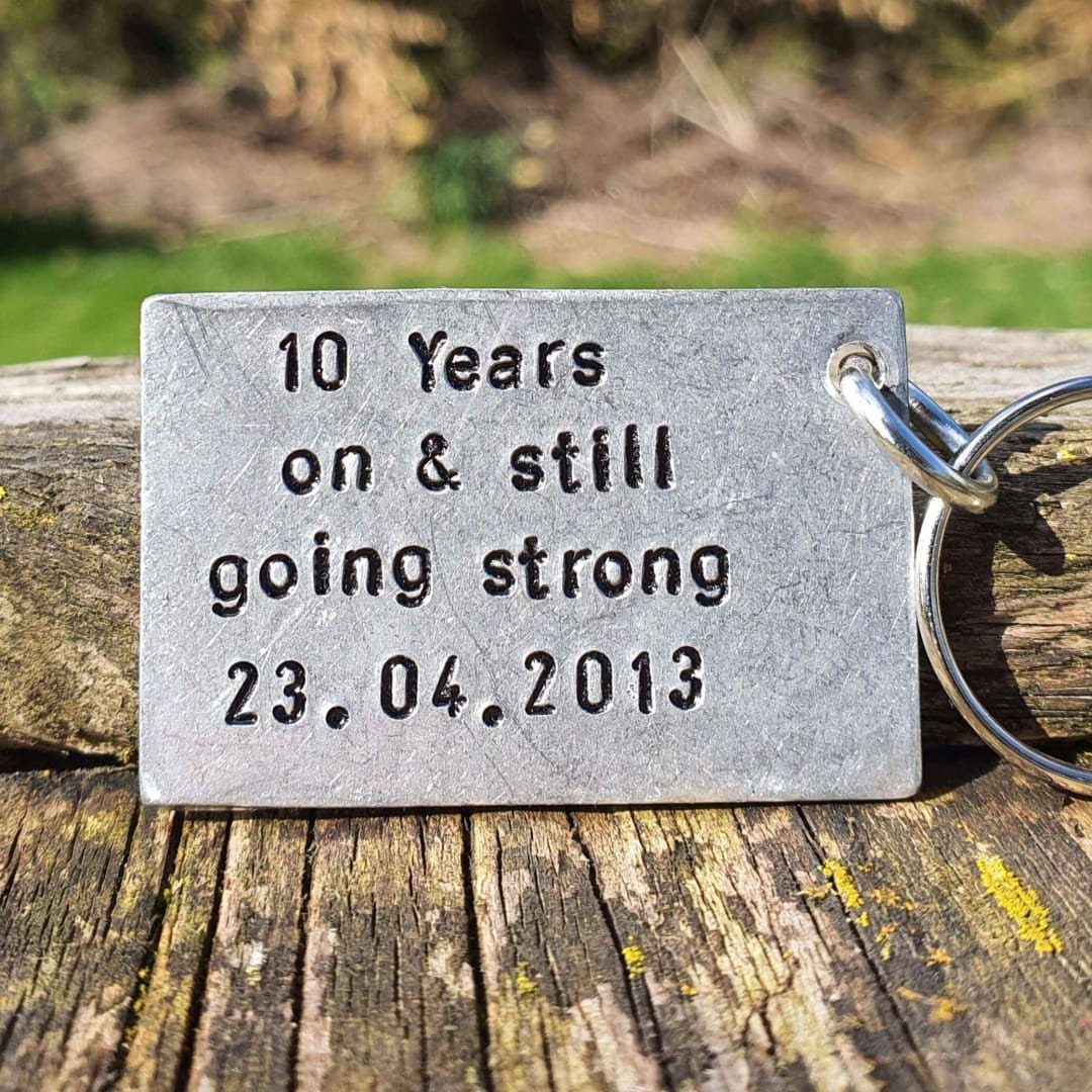 Stamped metal keychain tag with 10th anniversary message on a wooden beam