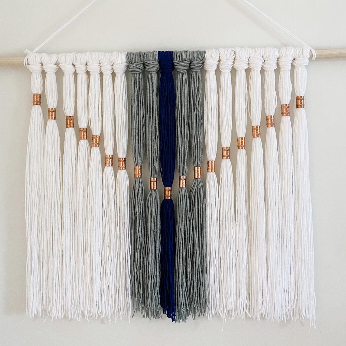 Macrame wall hanging with white and blue cords and copper metal bead accents.