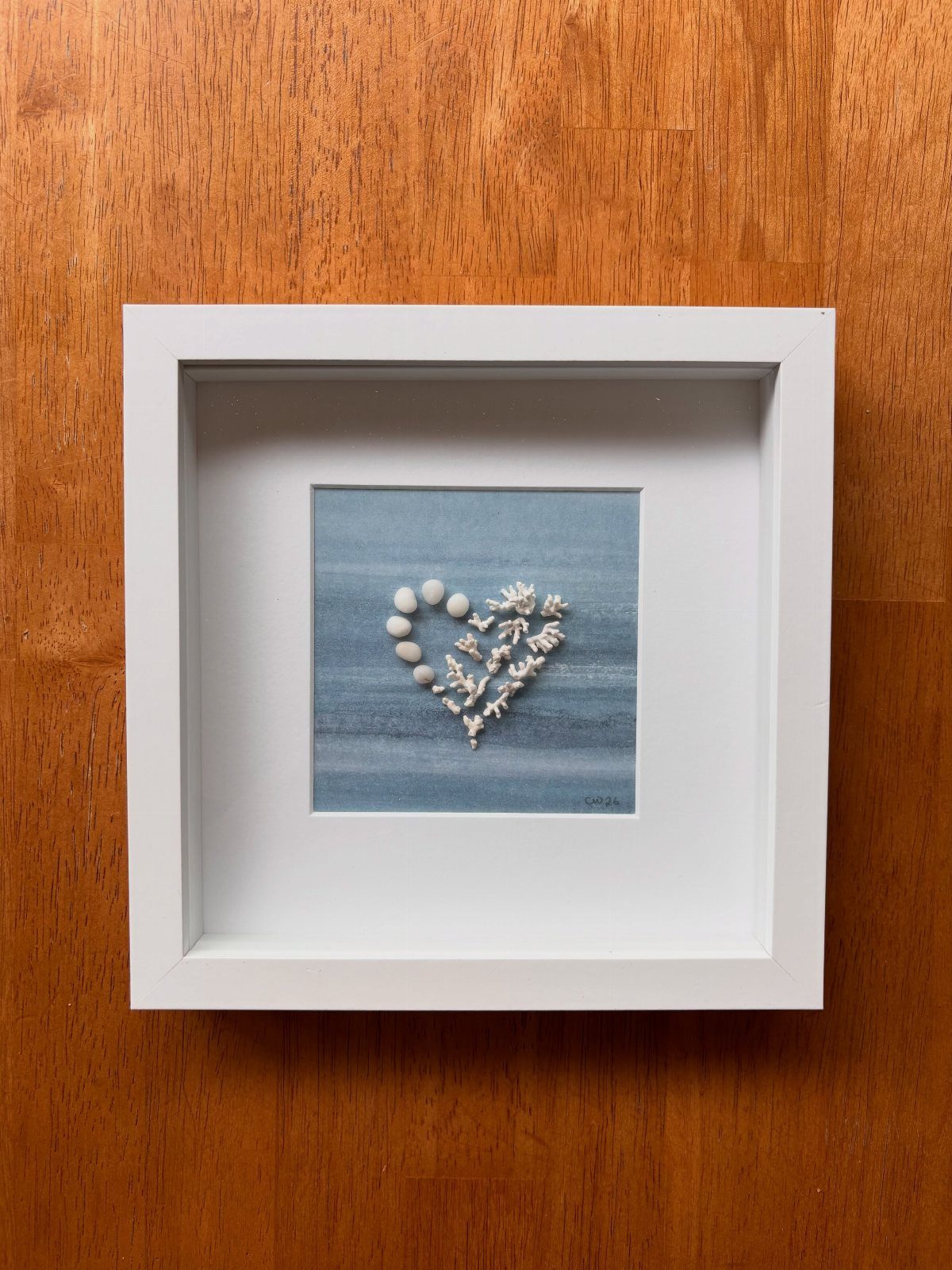 Heart shape made of white seashells and coral in a white shadow box