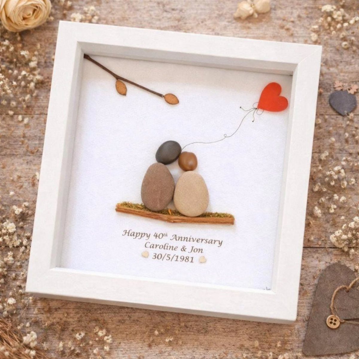 Pebble art of a couple holding a red heart balloon in a white frame