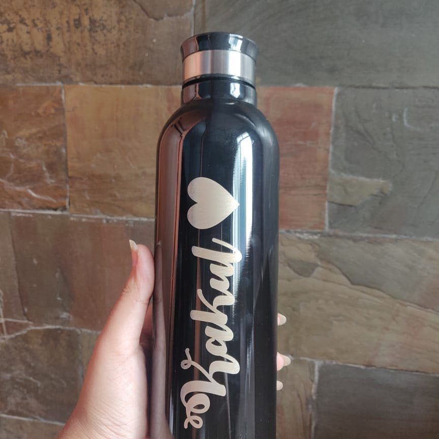 Black stainless steel water bottle with gold heart and name against stone wall
