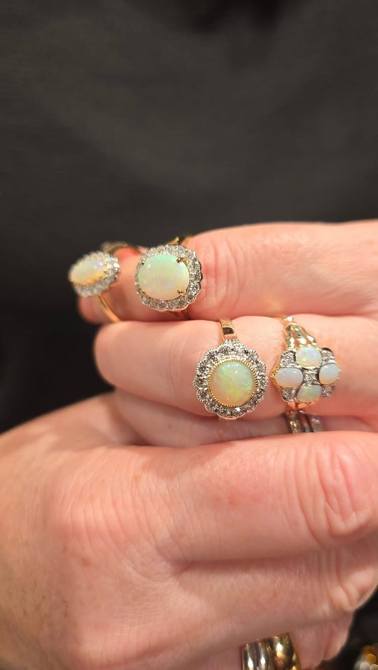 Four gold rings with iridescent opals and diamonds worn on a hand.