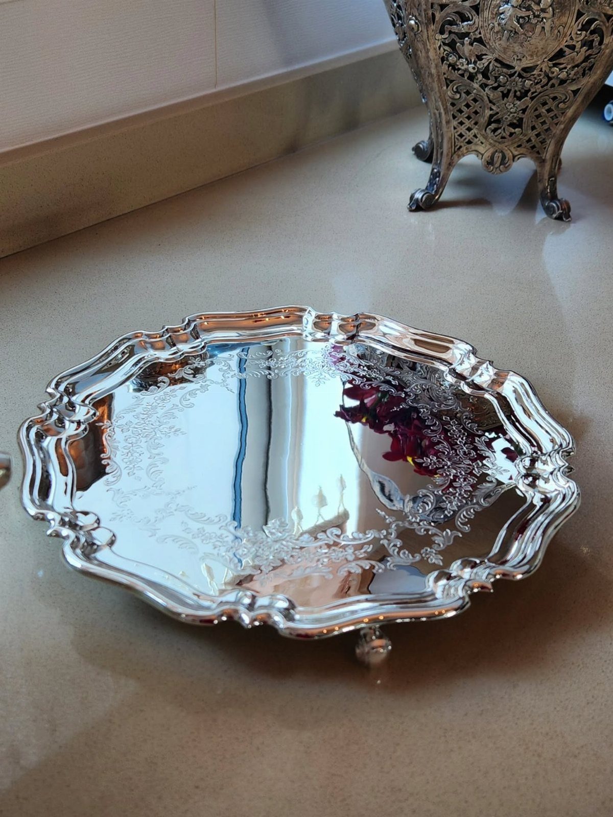 Silver-plated serving tray with ornate scalloped edges and floral engravings on a floor