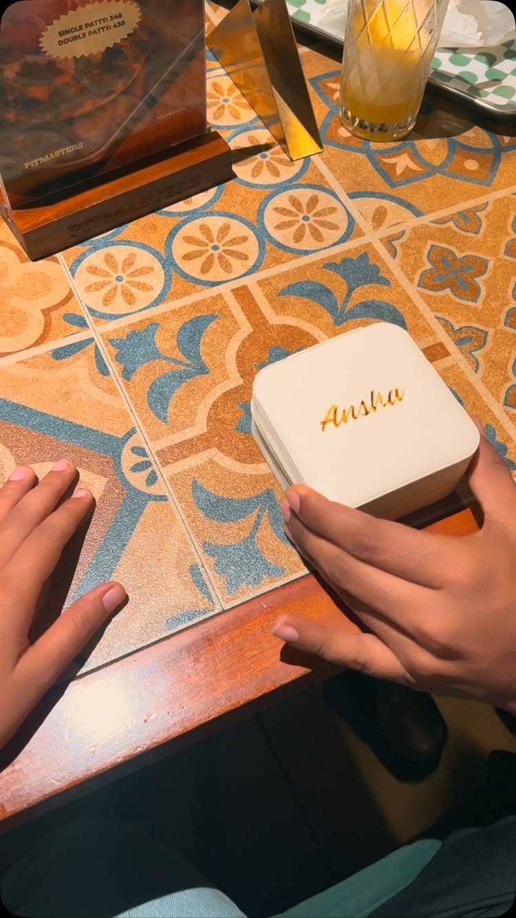 Small white jewelry box with gold name engraving held over a tiled table