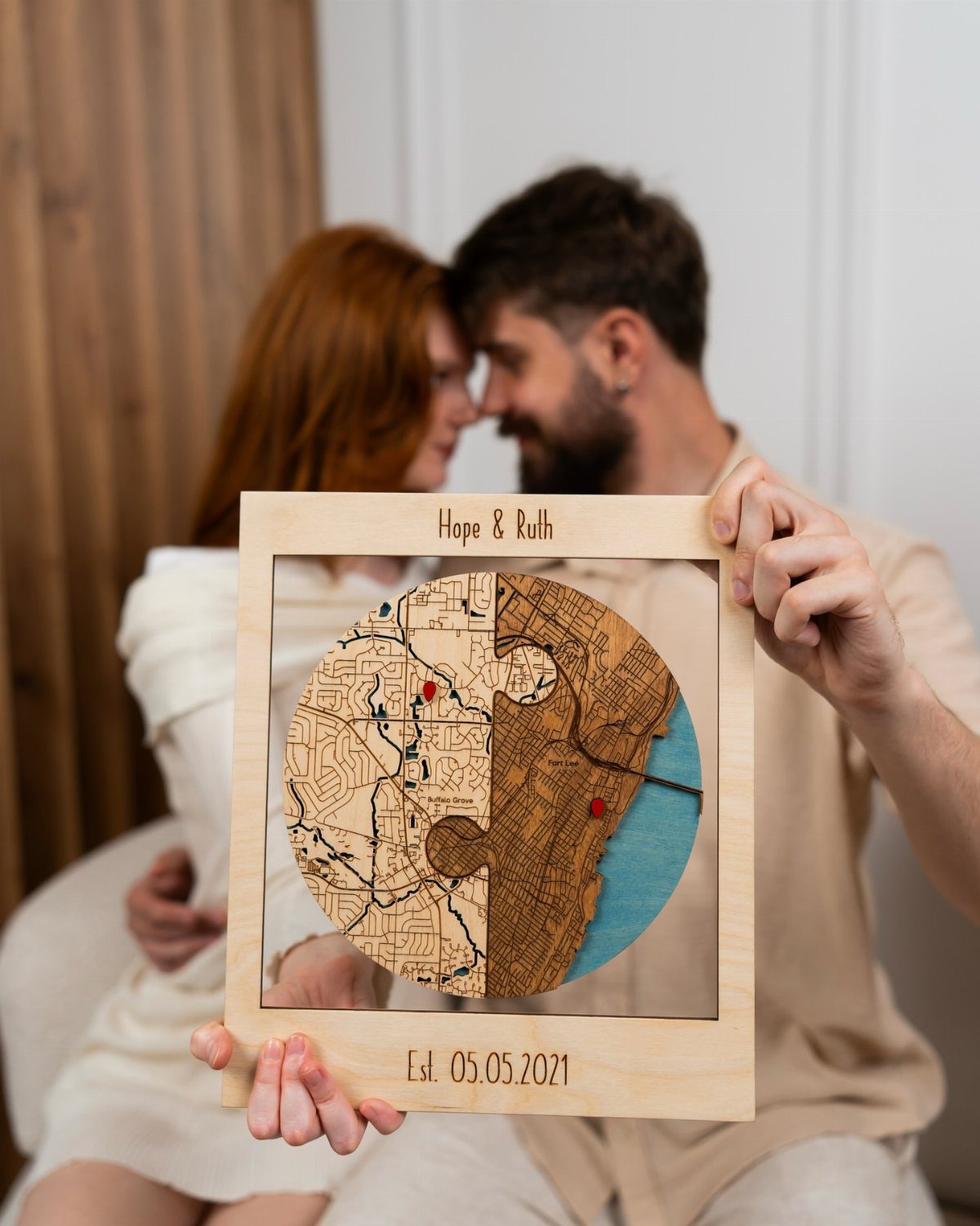 Couple holding a circular engraved wooden travel map with personalized names and date.