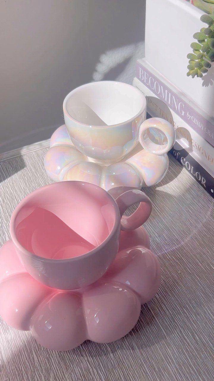 Two ceramic coffee cups with cloud-shaped saucers in iridescent white and pastel pink.
