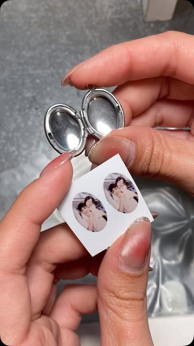 Small silver oval locket and tiny photos of a couple held by hands.