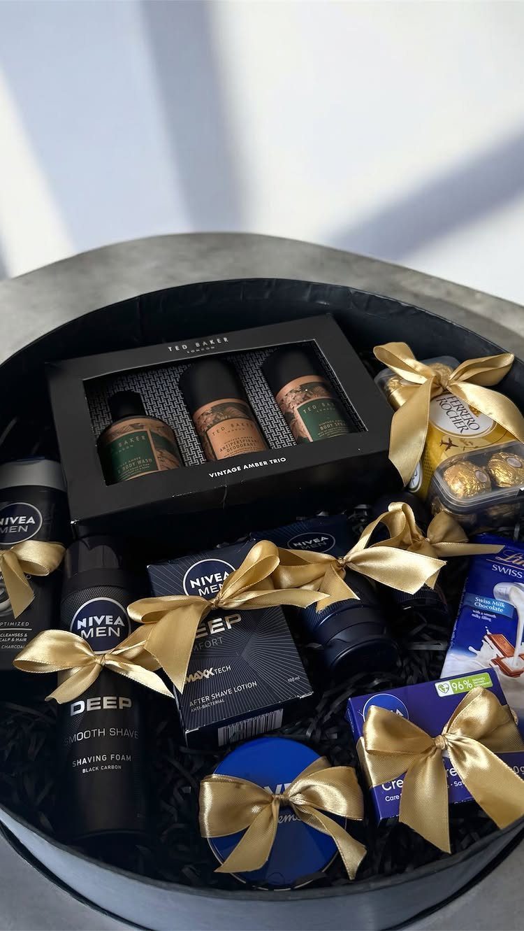 Black gift basket containing men's skincare, fragrances, and chocolates with gold ribbons.