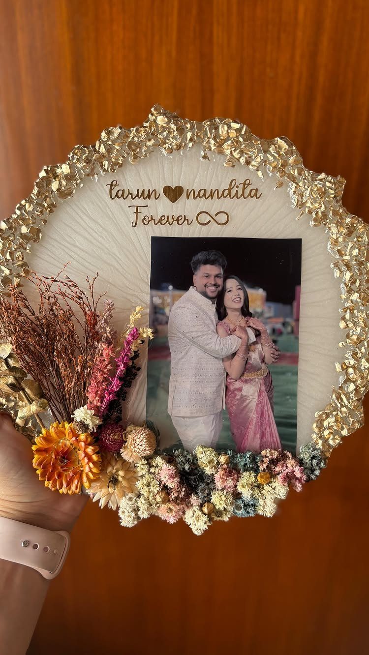 Circular white photo frame with gold border and dried flowers featuring a couple's photo.