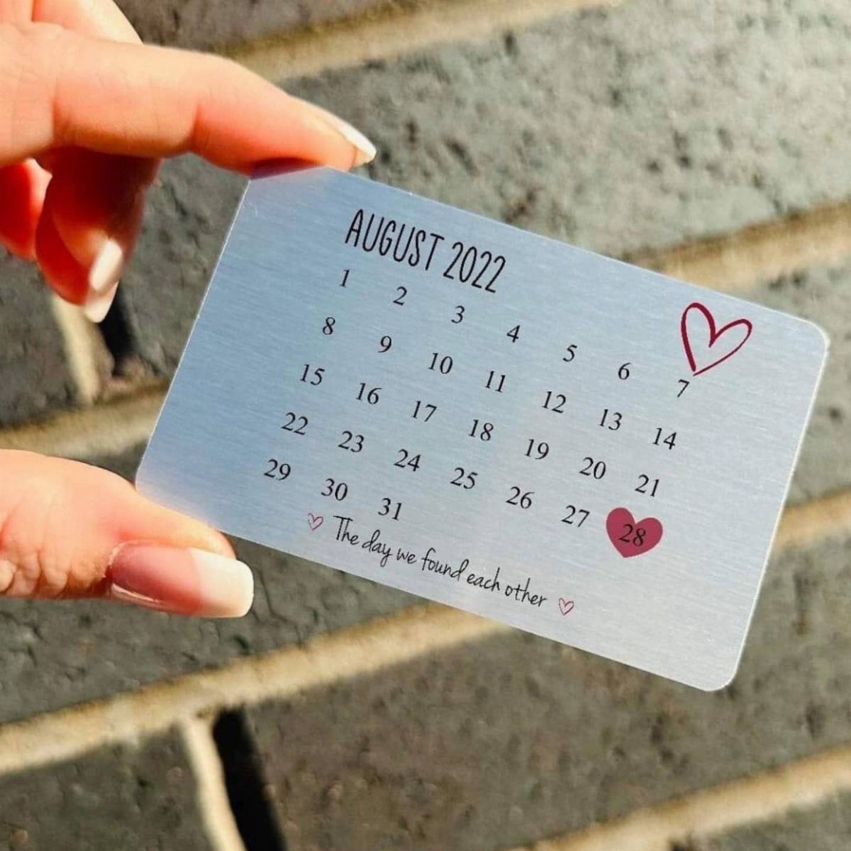 Metal calendar card with red hearts marking dates, held by a hand.