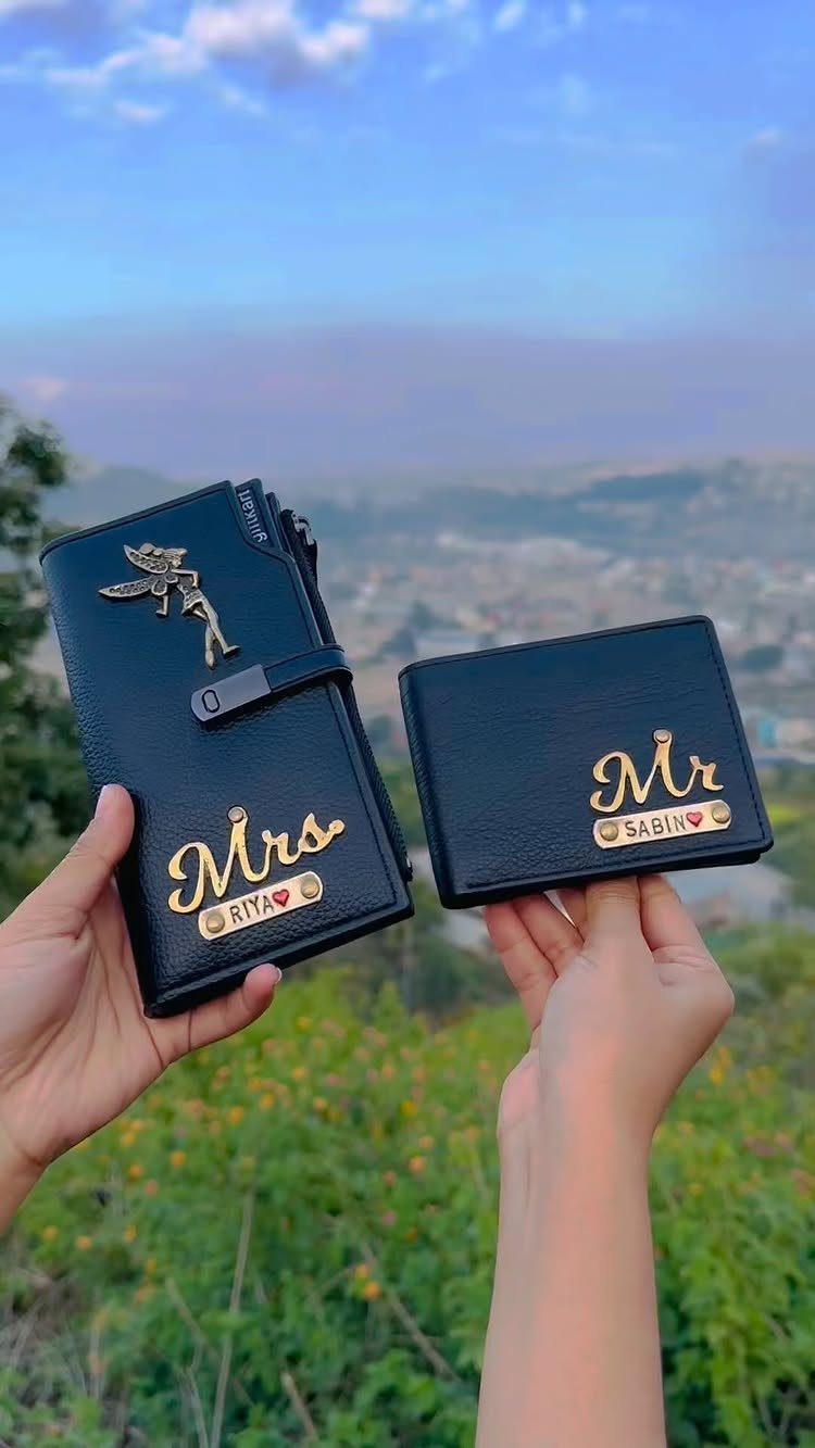 Two black leather wallets with gold personalized Mr and Mrs names held outdoors.