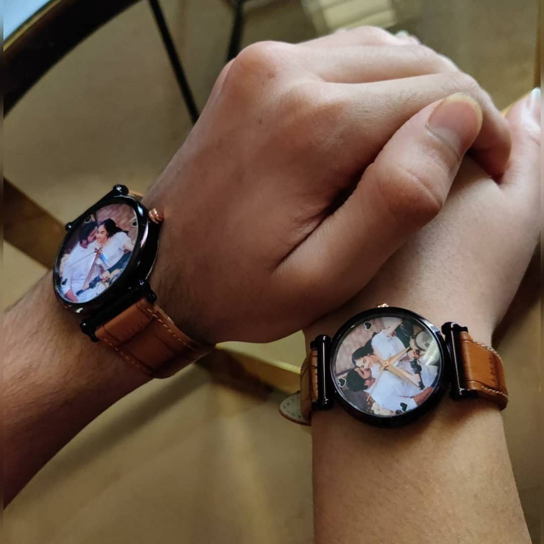 Two people holding hands wearing personalized watches with couple photos on the faces