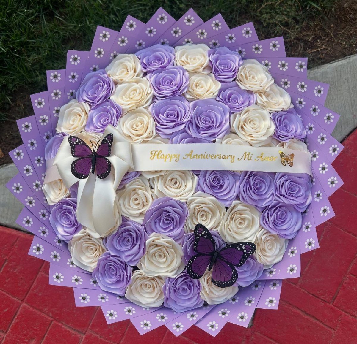 Round bouquet of purple and cream roses with butterflies and anniversary ribbon.